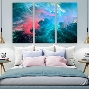 Op de afbeelding: Een drieluik wandkunstset met een abstracte explosie van levendig blauwgroen, diepblauw en felroze kleuren. De drie rechthoekige panelen tonen een dynamisch, wolkenachtig patroon met scherpe kleurovergangen en vloeiende, energieke penseelstreken.