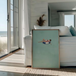 Pu&ograve; includere: Una stampa artistica rettangolare incorniciata con uno sfondo color verde acqua chiaro e una piccola illustrazione di una persona che indossa un costume da bagno rosa e occhiali da sole, galleggiante su un salvagente a righe blu e bianche.