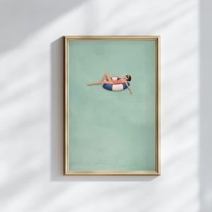 Pu&ograve; includere: Una stampa artistica da parete incorniciata che presenta un'illustrazione minimalista di una persona con costume da bagno rosso e occhiali da sole, che galleggia su un salvagente circolare a righe blu e bianche su sfondo verde chiaro.