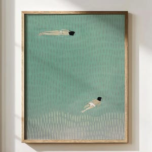 May include: A framed art print showing two figures swimming in a teal body of water. The figures are seen from above, with one near the top and the other near the bottom. The artwork is encased in a light brown wooden frame.