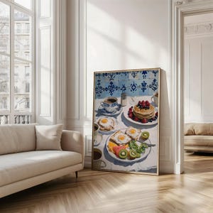 Puede incluir: Una impresi&oacute;n enmarcada de una escena de desayuno. La obra representa una mesa con panqueques, huevos, tostadas, fruta y caf&eacute;. El fondo presenta azulejos azules y blancos. La impresi&oacute;n est&aacute; en una habitaci&oacute;n luminosa con un sof&aacute;.