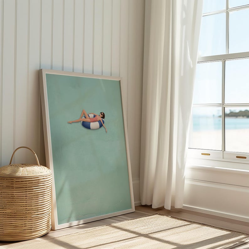 Pu&ograve; includere: Una stampa artistica incorniciata che presenta un'illustrazione minimalista di una persona con costume da bagno rosa e occhiali da sole, sdraiata su un salvagente gonfiabile a righe blu e bianche al centro di uno sfondo verde salvia tenue.
