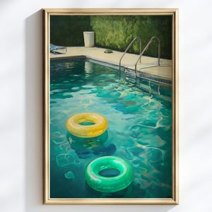 May include: A framed painting of a swimming pool with clear turquoise water. Two inflatable rings, one yellow and one green, float on the surface. A metal ladder leads into the pool. The painting is set in a gold frame.