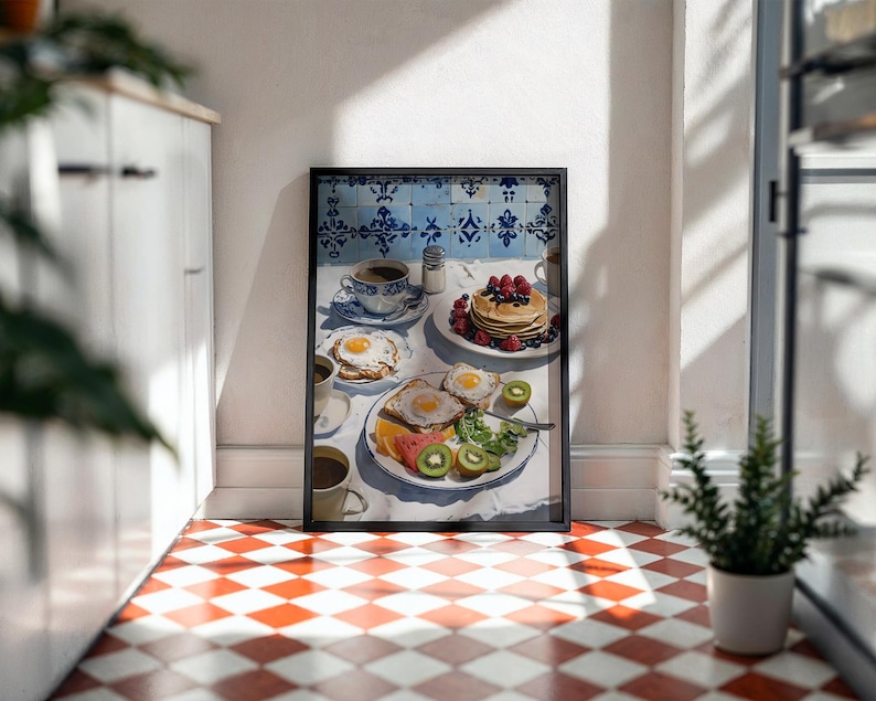 Puede incluir: Una impresi&oacute;n enmarcada de una escena de desayuno con panqueques con bayas, huevos fritos, tostadas, fruta y caf&eacute;. La obra de arte tiene un mantel blanco, azulejos azules y blancos y un marco negro. El suelo es a cuadros rojos y blancos.