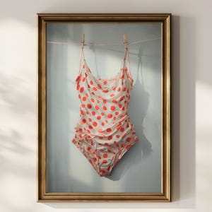 May include: A one-piece swimsuit featuring a white base with a vibrant red polka dot pattern. The garment has thin spaghetti straps, a draped cowl neckline, and gathered side detailing, all displayed hanging from a clothesline within a gold frame.