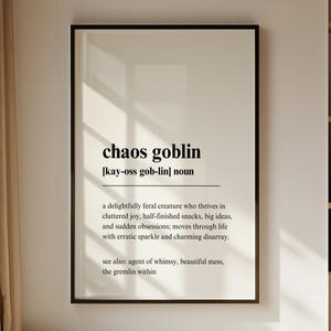 May include: A framed print on a wall with the words "chaos goblin" in a black font. The definition of "chaos goblin" is written below the title. The print is in a black frame.