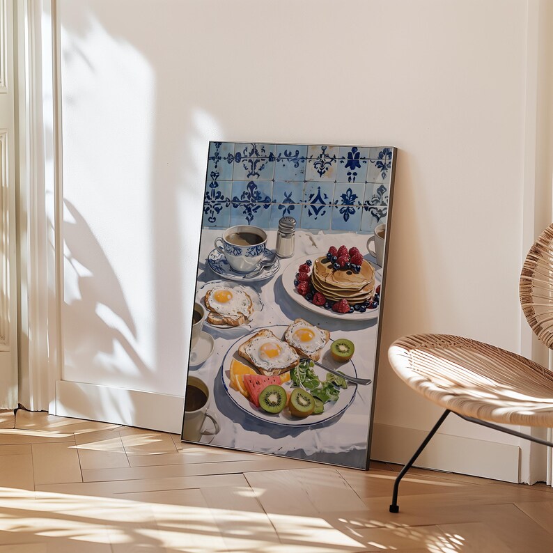 Puede incluir: Impresi&oacute;n enmarcada de una escena de desayuno con panqueques con bayas, huevos fritos, tostadas, fruta y caf&eacute;. La mesa est&aacute; puesta con un mantel blanco y vajilla con dise&ntilde;os azules y blancos. El fondo presenta azulejos azules y blancos.