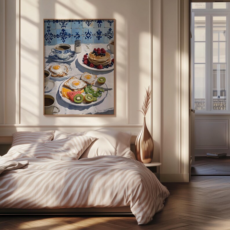 Puede incluir: Una pintura enmarcada representa una escena de desayuno con panqueques, huevos, fruta y caf&eacute;. La mesa est&aacute; puesta con platos y tazas, y el fondo presenta azulejos azules y blancos. La obra de arte se exhibe sobre una cama con ropa de cama a rayas.