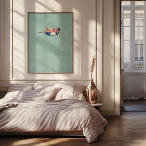 Pu&ograve; includere: Una stampa d'arte da parete incorniciata che raffigura una persona in costume da bagno rosa e occhiali da sole che galleggia su un salvagente a righe blu e bianche in una piscina verde chiaro. L'opera &egrave; esposta sopra un letto con biancheria a righe.