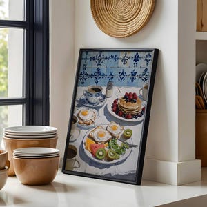 Puede incluir: Una impresi&oacute;n enmarcada de una escena de desayuno con panqueques, huevos, fruta y caf&eacute;. La obra de arte tiene un fondo de azulejos azules y blancos. La imagen est&aacute; ambientada en una cocina con cuencos y platos.