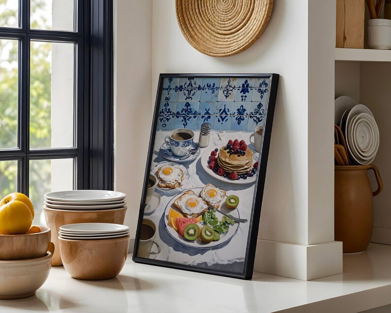 Puede incluir: Una impresi&oacute;n enmarcada de una escena de desayuno con panqueques, huevos, fruta y caf&eacute;. La obra de arte tiene un fondo de azulejos azules y blancos. La imagen est&aacute; ambientada en una cocina con cuencos y platos.
