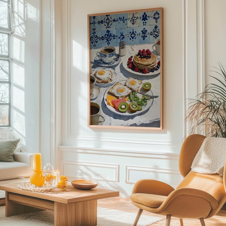 Puede incluir: Una impresi&oacute;n enmarcada de una escena de desayuno. La obra de arte representa una mesa con panqueques, huevos, fruta, caf&eacute; y un fondo con patrones azules y blancos. La pintura est&aacute; en una habitaci&oacute;n luminosa con un marco de madera.