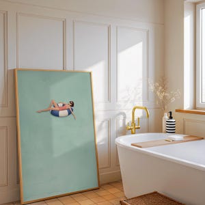 Pu&ograve; includere: Una stampa artistica da parete incorniciata con un'illustrazione minimalista di una figura in costume da bagno rosa e occhiali da sole che si rilassa su un salvagente a righe blu e bianche, su sfondo verde salvia in cornice di legno chiaro.