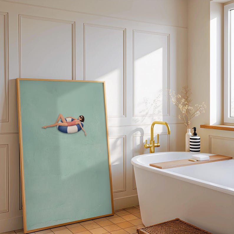 Pu&ograve; includere: Una stampa artistica da parete incorniciata con un'illustrazione minimalista di una figura in costume da bagno rosa e occhiali da sole che si rilassa su un salvagente a righe blu e bianche, su sfondo verde salvia in cornice di legno chiaro.