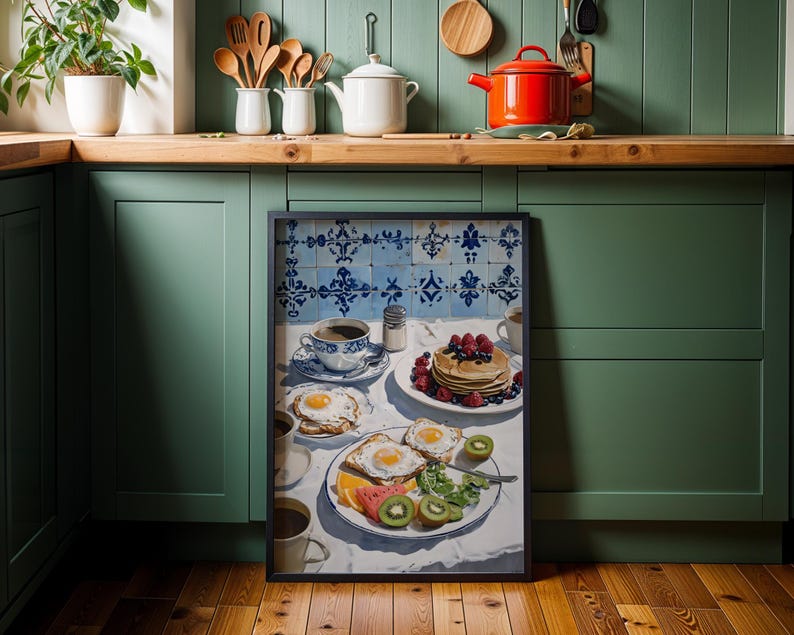 Puede incluir: Una impresi&oacute;n enmarcada de una escena de desayuno con panqueques, huevos, fruta y caf&eacute;. La obra de arte est&aacute; ambientada sobre un fondo de azulejos azules y blancos. La cocina tiene gabinetes verdes y encimeras de madera.