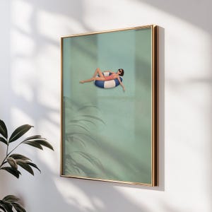 Pu&ograve; includere: Una stampa artistica incorniciata che raffigura una persona con costume da bagno rosa e occhiali da sole, che galleggia su un salvagente a righe blu e bianche in una piscina verde chiaro. L'opera &egrave; racchiusa in una sottile cornice color oro.