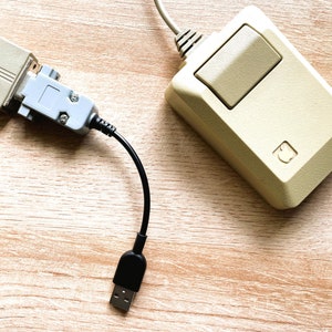 May include: A black USB to PS/2 adapter cable connected to a beige Apple Macintosh mouse with a single button.