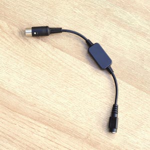 Pode incluir: Um adaptador de cabo de áudio preto com um conector retangular e um conector de 3,5 mm.