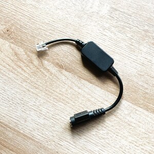 May include: A black telephone adapter with a RJ-11 connector on one end and a modular connector on the other end.