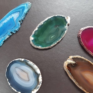 Puede incluir: Cinco rebanadas de ágata en varios colores y patrones. Las rebanadas son todas de forma ovalada y tienen un acabado natural y pulido. Los colores incluyen azul, verde, rosa, marrón y gris.