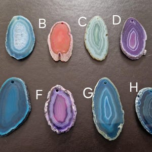 May include: Eight polished agate slices in various colors, including blue, pink, green, and purple. Each slice has a hole drilled at the top for stringing. The stones display concentric banding patterns, showcasing natural mineral formations.