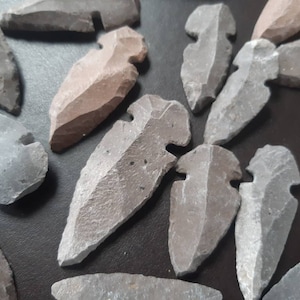 May include: A collection of gray and brown arrowheads made of stone. The arrowheads are various sizes and shapes, with some having a pointed tip and others having a rounded tip.