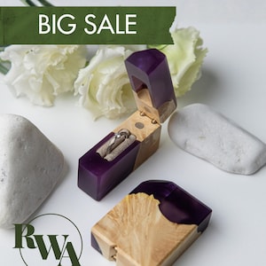 Può includere: Un portaanelli rettangolare in legno chiaro e resina viola traslucida, con coperchio incernierato e interno in velluto beige contenente un anello argentato con una piccola pietra. Il testo BIG SALE è visibile in alto.