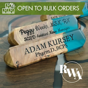 Op de afbeelding: Houten naamlabels met turquoise harsaccenten. De labels zijn gegraveerd met namen en titels, waaronder "Peggy Weeks, MSX, RX" en "Adam Kursey, Pharm.D., BCPS." De afbeelding bevat ook de tekst "OPEN TO BULK ORDERS."