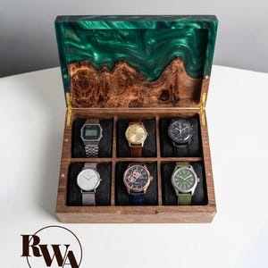 May include: A wooden watch box with a green epoxy resin lid and six watches. The box is made of dark wood and has a hinged lid. The watches are in various styles, including digital and analog, with metal, leather, and fabric bands.