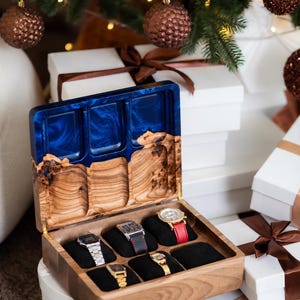 May include: A wooden watch box with a hinged lid featuring a blue resin inlay. The interior has six black velvet slots, five of which contain wristwatches with various metal and leather bands. The lid interior has three carved wooden compartments.