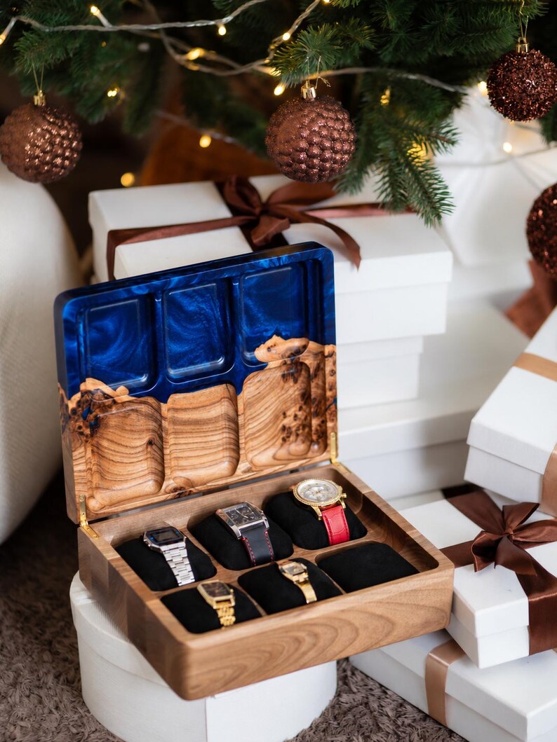 May include: A wooden watch box with a hinged lid featuring a blue resin inlay. The interior has six black velvet slots, five of which contain wristwatches with various metal and leather bands. The lid interior has three carved wooden compartments.
