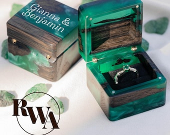 Puede incluir: Dos joyeros de madera hechos a mano con detalles de resina verde esmeralda. Una caja está abierta, revelando un anillo sobre un interior de terciopelo negro. Las tapas de las cajas están grabadas con los nombres "Gianna & Benjamin".