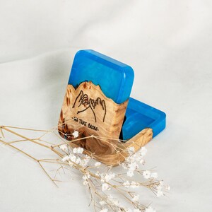 Op de afbeelding: Een rechthoekige houten doos met een felblauw hars bovendeel. Het hout heeft een natuurlijke nerf en een ingebrande illustratie van twee handen die een pinkbelofte maken met de tekst "NO TAKE BACKS" onder de handen geschreven.