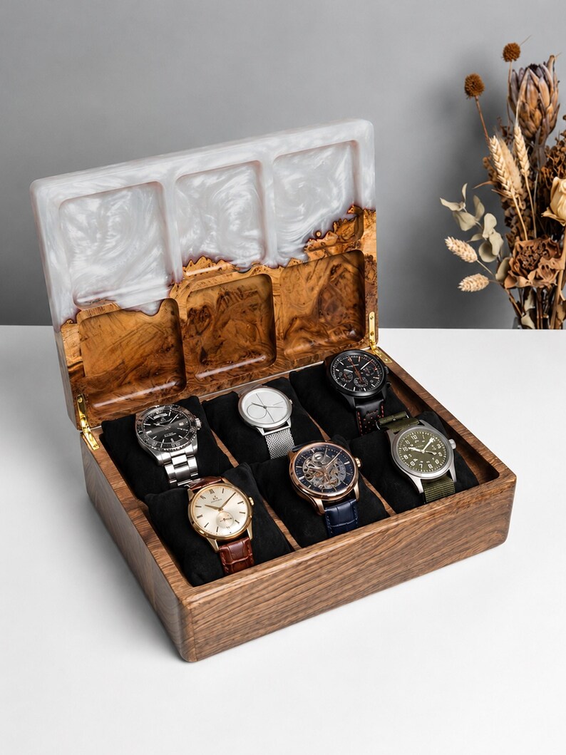 May include: A rectangular wooden watch box with a hinged lid featuring a white marbled resin inlay. The interior contains six black velvet cushions, each holding a different wristwatch with various metal, leather, and fabric straps.