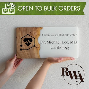 May include: A rectangular sign featuring a natural wood grain section on the left and a smooth white surface on the right. The wood side displays a black heart icon with an EKG line. The white side reads Green Valley Medical Center, Dr. Michael Lee, MD, Cardiology.
