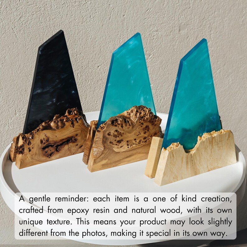 May include: Three unique decorative pieces. Each features a triangular epoxy resin element in black and teal, set atop a natural wood base. The wood has a distinctive, textured grain. The text in the image says: "A gentle reminder: each item is a one of kind creation..."