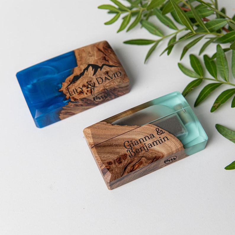 May include: Two rectangular wooden cases with resin accents. One case has blue resin and the text "Lily & David". The other case has teal resin and the text "Gianna & Benjamin". Both cases have a mountain graphic.