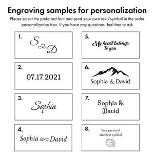 May include: Image showcasing engraving samples for personalization. The image displays various text and symbol options, including initials, dates, names, and phrases like "My heart belongs to you." It also includes a mountain graphic and a space for a personal sketch or symbol.