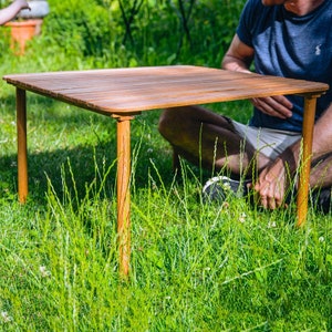 Könnte beinhalten: Ein Holztisch mit einer Lattenoberfläche steht auf einem Rasen. Der Tisch ist braun und hat vier Beine.