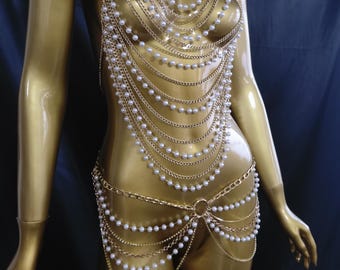 Può includere: Catena da corpo dorata con più fili di perle finte e delicate maglie a catena. Il gioiello per il corpo drappeggia sul busto e sui fianchi, creando un effetto a strati. Il design include uno scollo all'americana e una catena in vita con un connettore circolare.