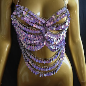 May include: An iridescent purple sequin top with a halter neck and chain detailing. The top features multiple layers of cascading sequins, creating a glamorous effect. The sequins are in shades of purple and pink. The top is a statement piece.