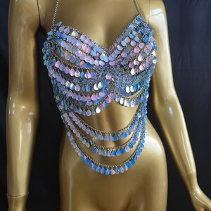 May include: A halter-style body chain top constructed from silver-toned metal links and iridescent, teardrop-shaped sequins. The garment features a multi-layered design with cascading rows of shimmering, light-reflecting scales that drape over the torso.