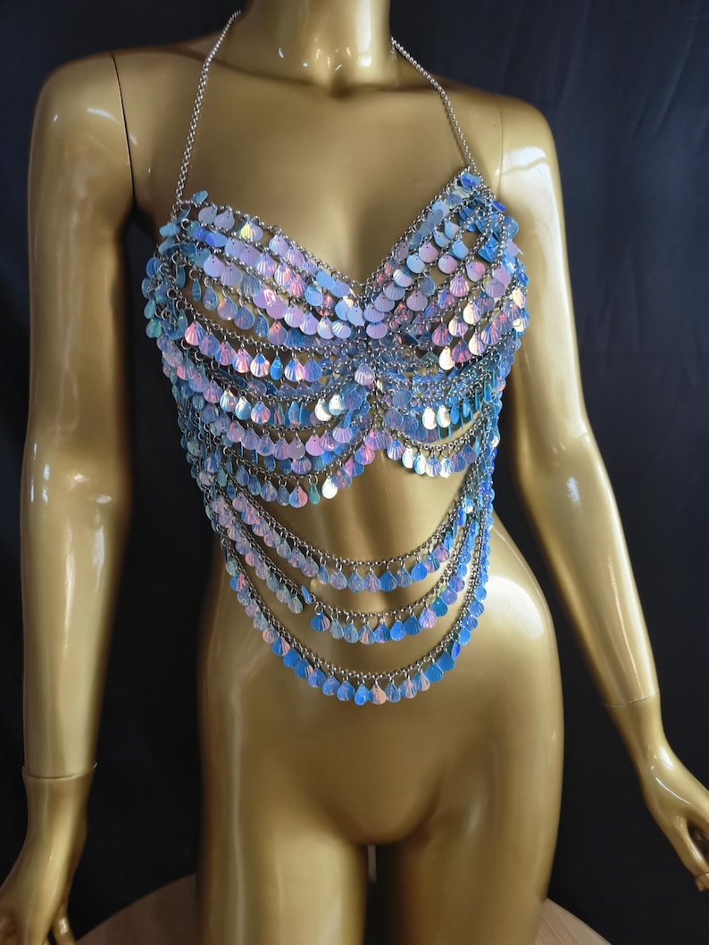 May include: A halter-style body chain top constructed from silver-toned metal links and iridescent, teardrop-shaped sequins. The garment features a multi-layered design with cascading rows of shimmering, light-reflecting scales that drape over the torso.