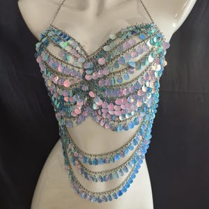 May include: A halter-style body chain top constructed from silver-toned metal links and iridescent, light-reflecting circular sequins. The garment features multiple draped layers of chains and sequins that form a scalloped, fringe-like pattern.