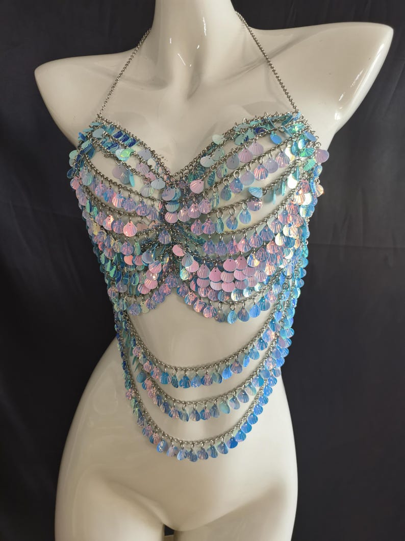 May include: A halter-style body chain top constructed from silver-toned metal links and iridescent, light-reflecting circular sequins. The garment features multiple draped layers of chains and sequins that form a scalloped, fringe-like pattern.
