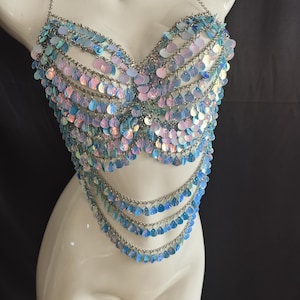 May include: A halter-style body chain top constructed from silver-toned metal links and adorned with numerous iridescent, light blue, and pink circular sequins. The garment features a structured bodice section and three cascading lower chain layers.