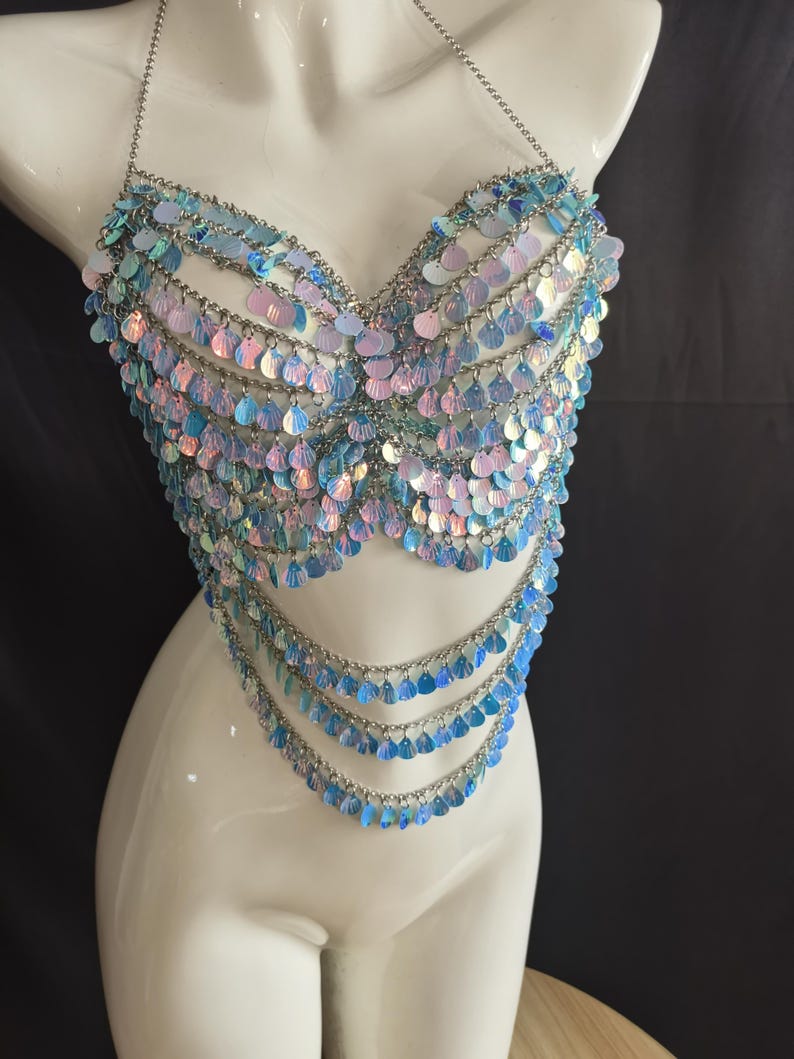 May include: A halter-style body chain top constructed from silver-toned metal links and adorned with numerous iridescent, light blue, and pink circular sequins. The garment features a structured bodice section and three cascading lower chain layers.