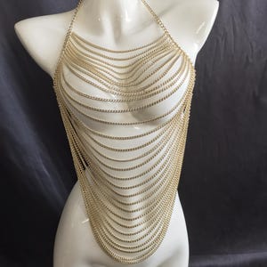 May include: Gold-colored chainmail top. The halter-style top is made of multiple strands of delicate chains that cascade down in a layered design. The chains are draped over a white mannequin.