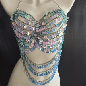 May include: A halter-style top constructed from silver-toned metal chains and iridescent, teardrop-shaped sequins. The garment features multiple draped layers of shimmering blue and pink scales that create a textured, reflective surface across the chest.