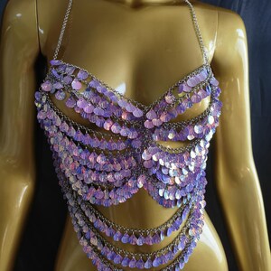 May include: A halter-style body chain top constructed from silver-toned metal links. The garment features multiple cascading rows of iridescent, light purple, shell-shaped sequins that shimmer with a pearlescent finish across the chest and torso.